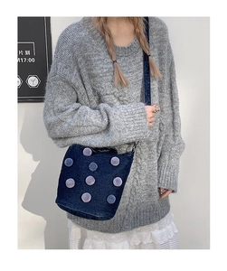 Detail of dark blue denim tote with grey plush pom-poms shown on shoulder strap