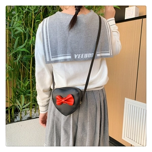 Detail shot of a heart-shaped girls' crossbody bag with red bow on a child model
