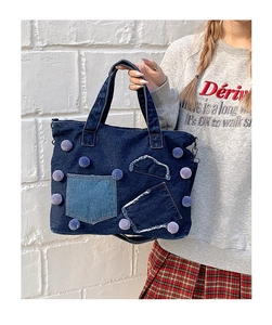 Dettaglio borsa tote in denim blu con pompon viola e tasche patchwork decorative