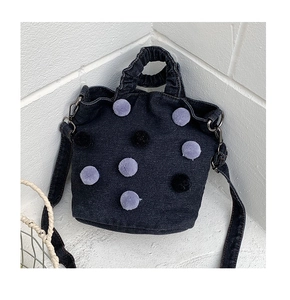 Detail of dark blue denim bucket bag with plush pom-poms and silver hardware finish