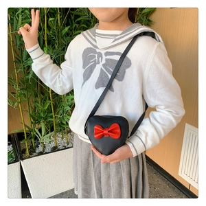 Close-up of heart-shaped black crossbody bag with red bow worn by child model