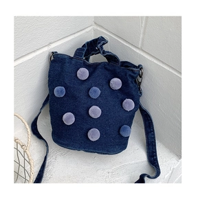 Detail of dark blue denim tote bag featuring purple plush pom poms and shoulder strap