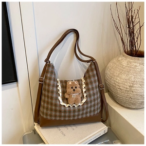 Detail of checkered crossbody bag with cute plush bear charm on home lifestyle setting