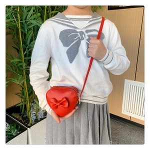 Close-up of a red heart-shaped kids crossbody bag featuring a 3D bow and slim strap