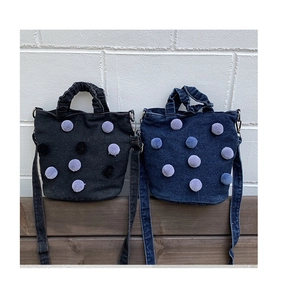 Detailed view of blue and black denim bucket bags with white pom-pom decorations
