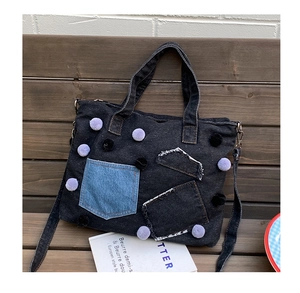 Dettaglio borsa tote in denim nero con pompon viola e tasca applicata azzurra