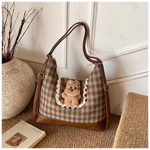 Detail of plaid kids crossbody bag featuring brown leather base and plush bear charm