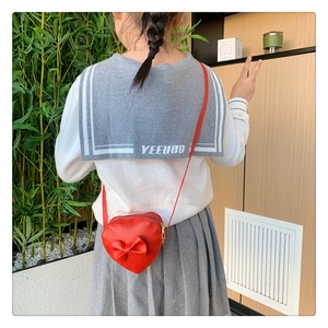 Detail of red heart-shaped girls shoulder bag with bow and gold zipper on model