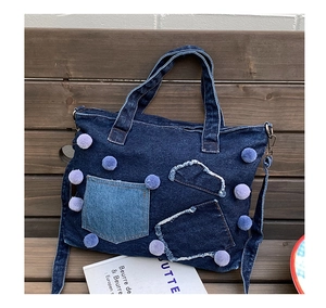 Dettaglio della borsa in denim con pompon lavanda e tasche su una panca di legno