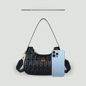 Detail showing black quilted hobo bag with gold hardware and phone for size comparison