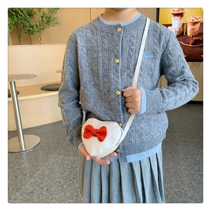 White heart-shaped crossbody bag with a large red bow shown on a child's outfit