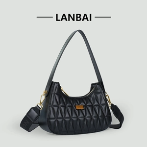 Close-up of black quilted dumpling bag with gold metal logo and wide woven strap
