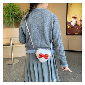 Detailed view of child wearing white heart-shaped crossbody bag with red bow accent