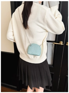 Detail of light blue mini shell bag with silver chain strap on a white sweater