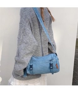 Détail d'un sac messager en denim bleu clair avec sangles à boucle porté par un mannequin