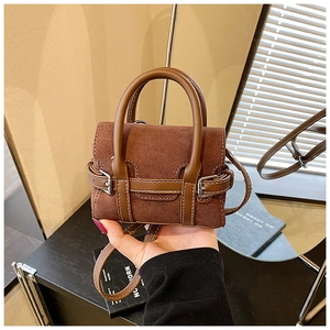 Detail of brown suede mini handbag with metal buckle accents and adjustable shoulder strap