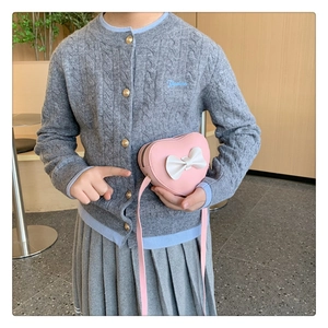 Close-up of pink heart-shaped crossbody bag with a white bow on a girl's sweater
