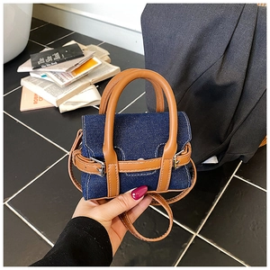 Close-up of mini Boston-style denim shoulder bag with brown leather handles and straps