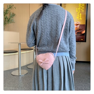 Detail of pink heart-shaped girls crossbody bag with bow worn by child model