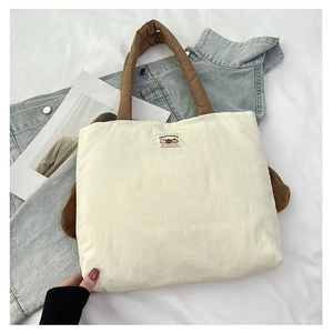 Close-up of cream tote bag with quilted brown handles and embroidered logo patch detail