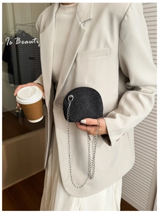 Detail of a black sequined shell chain bag held by a model in a minimalist urban setting