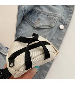 Close-up of a mini white canvas coin purse with black handles held against denim