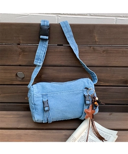 Détail du sac bandoulière en jean bleu clair avec gland étoile sur fond de bois