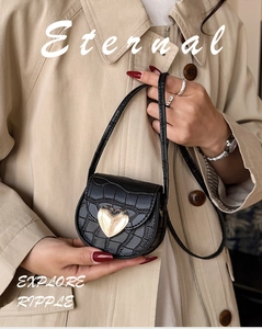 Gros plan sur un mini sac besace noir effet crocodile avec boucle cœur en métal doré
