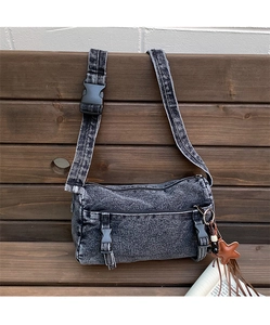 Détail du sac cylindrique en jean délavé gris foncé avec pendentif étoile et pompons