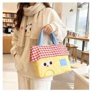 Close-up of a house-shaped yellow canvas bag with red checkered roof and blue handles