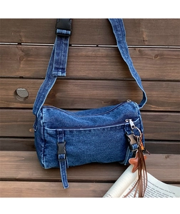 Gros plan du sac bandoulière en denim bleu avec boucle noire et pompon étoile en cuir