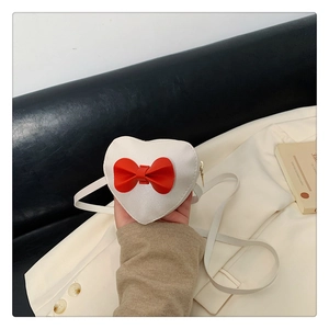 Detail of a heart-shaped white crossbody bag for girls with a red 3D bow and PU leather texture