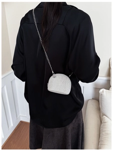 Close-up of a silver glitter mini shell bag with a delicate metal chain strap on a model