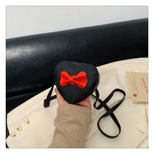 Close-up of heart-shaped crossbody bag with a red bow on black PU leather