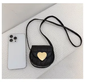 Mini sac bandoulière noir effet crocodile avec boucle cœur à côté d'un smartphone