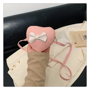 Close-up of pink heart-shaped mini crossbody bag with a white bow and gold zipper