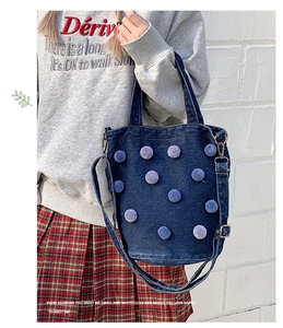 Detail of blue denim bucket bag featuring purple pom-pom accents and adjustable shoulder strap