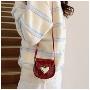 Détail du mini sac selle rouge à texture crocodile et fermoir cœur doré sur modèle