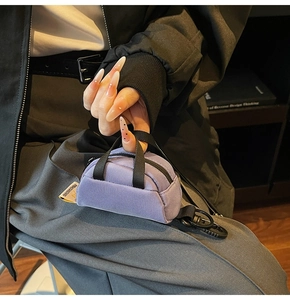 Detail of purple mini suitcase pouch with black strap and hook held by a model