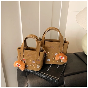 Detalle del bolso tote marrón para niños con bordados, colgante de oso y asas suaves