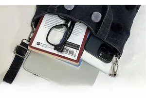 Top view of black denim bucket bag interior with pom-pom detail holding a phone and glasses
