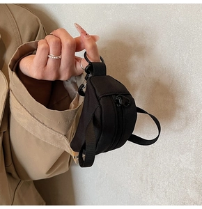 Miniature black utility-style backpack coin purse charm held by hand against a coat