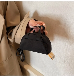 Mini black canvas pendant bag with yellow label shown held in hand against a beige coat
