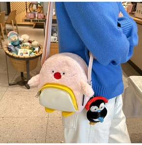 Rosa Plüsch-Pinguin-Umhängetasche mit süßem Anhänger auf blauem Strickpullover-Hintergrund