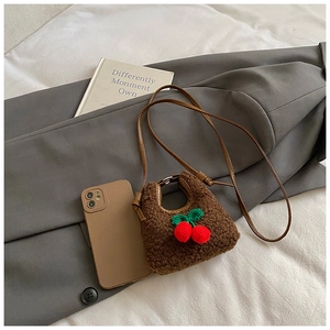 Close-up of brown plush crossbody bag with red cherry charm and matching phone case