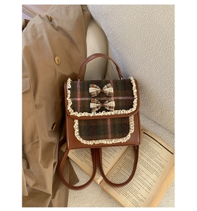 Detail of vintage brown plaid backpack with lace trim and bows on a beige coat