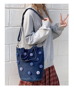 Detail of dark blue denim bucket bag with colorful plush balls and adjustable shoulder strap