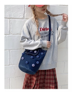 Detail of dark blue denim bucket bag featuring purple pom-pom accents and strap texture