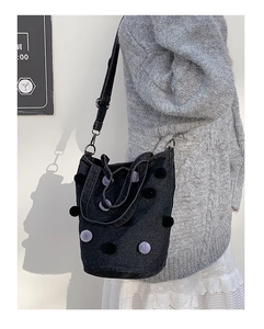 Detail of dark denim bucket bag with plush pom-pom charms and adjustable strap