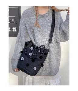 Detail of denim bucket bag with plush pom-poms worn by a model in casual attire